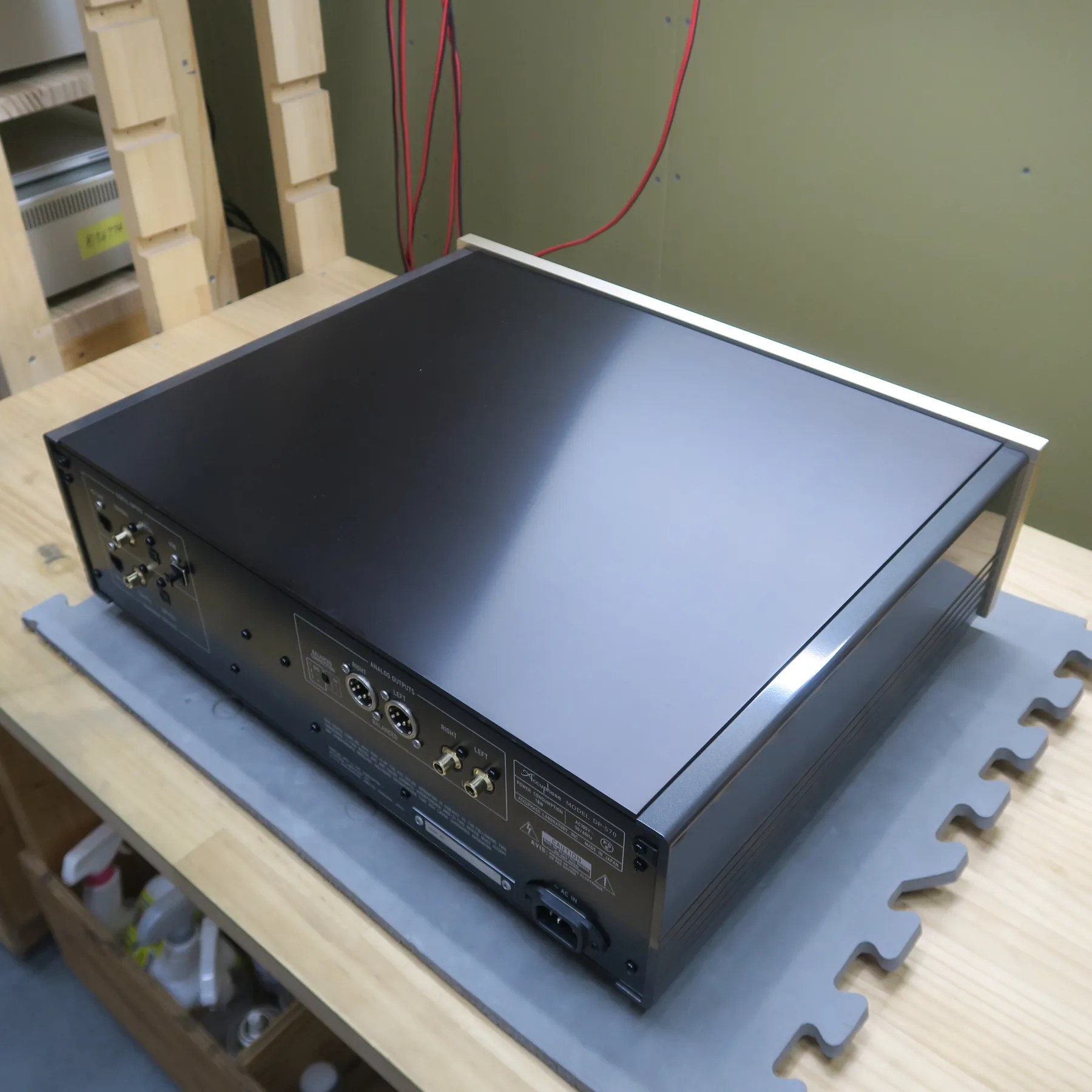 アキュフェーズ DP-570 CDデッキの斜め後ろから見た外観、横長の直方体筐体、天板は黒色光沢素材、側面はグレーの金属製マット仕上げ 背面は黒色金属パネルでアナログ出力、電源入力端子が見える 天板周囲にシャンパンゴールドの金属フレーム