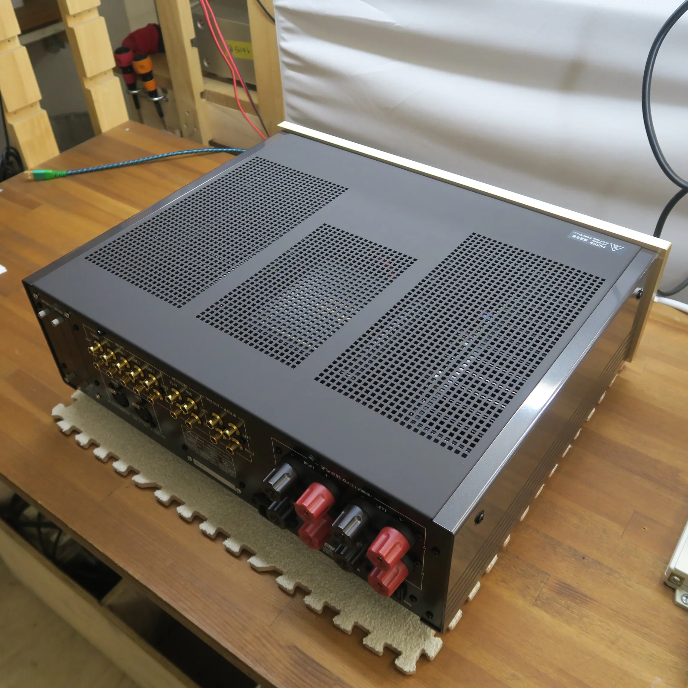 アキュフェーズ E-3000 プリメインアンプの斜め後ろから見た外観、濃いグレーの金属筐体、天板は多数の通気孔、前面上部にシャンパンゴールドのバー、側面は放熱フィン